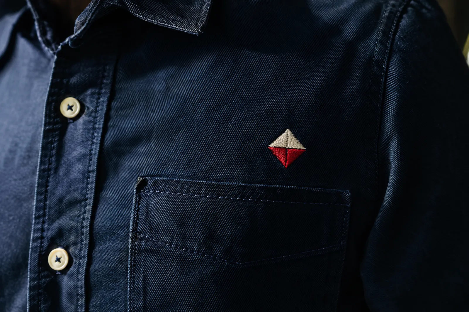Camisa azul marino de manga larga con un emblema rojo bordado arriba de la bolsa del pecho izquierdo